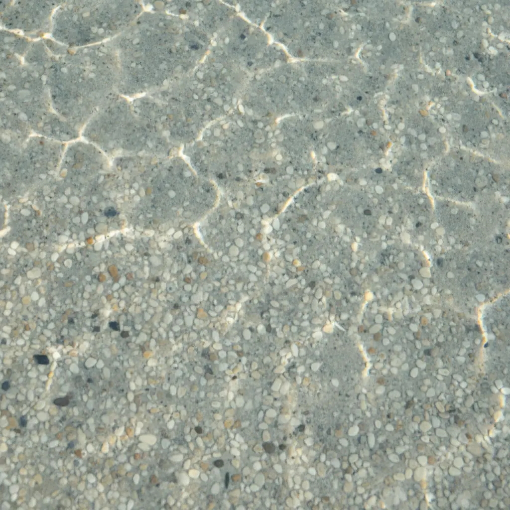Close-up of a quartz pebble pool interior under clear water with sunlight patterns
